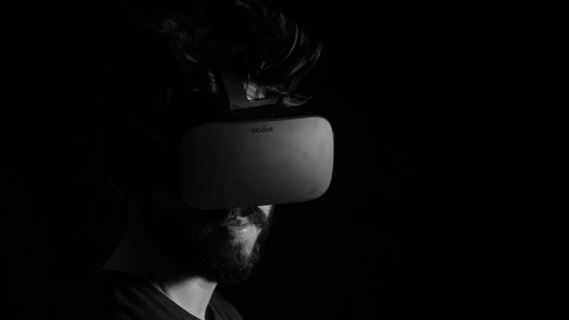 Hand holding a modern VR controller in a dimly lit gaming room with motion-tracked lights